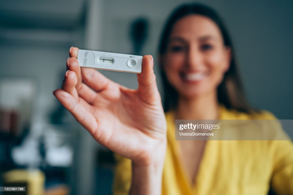 Woman in yellow shirt holding a negative rapid COVID-19 test.