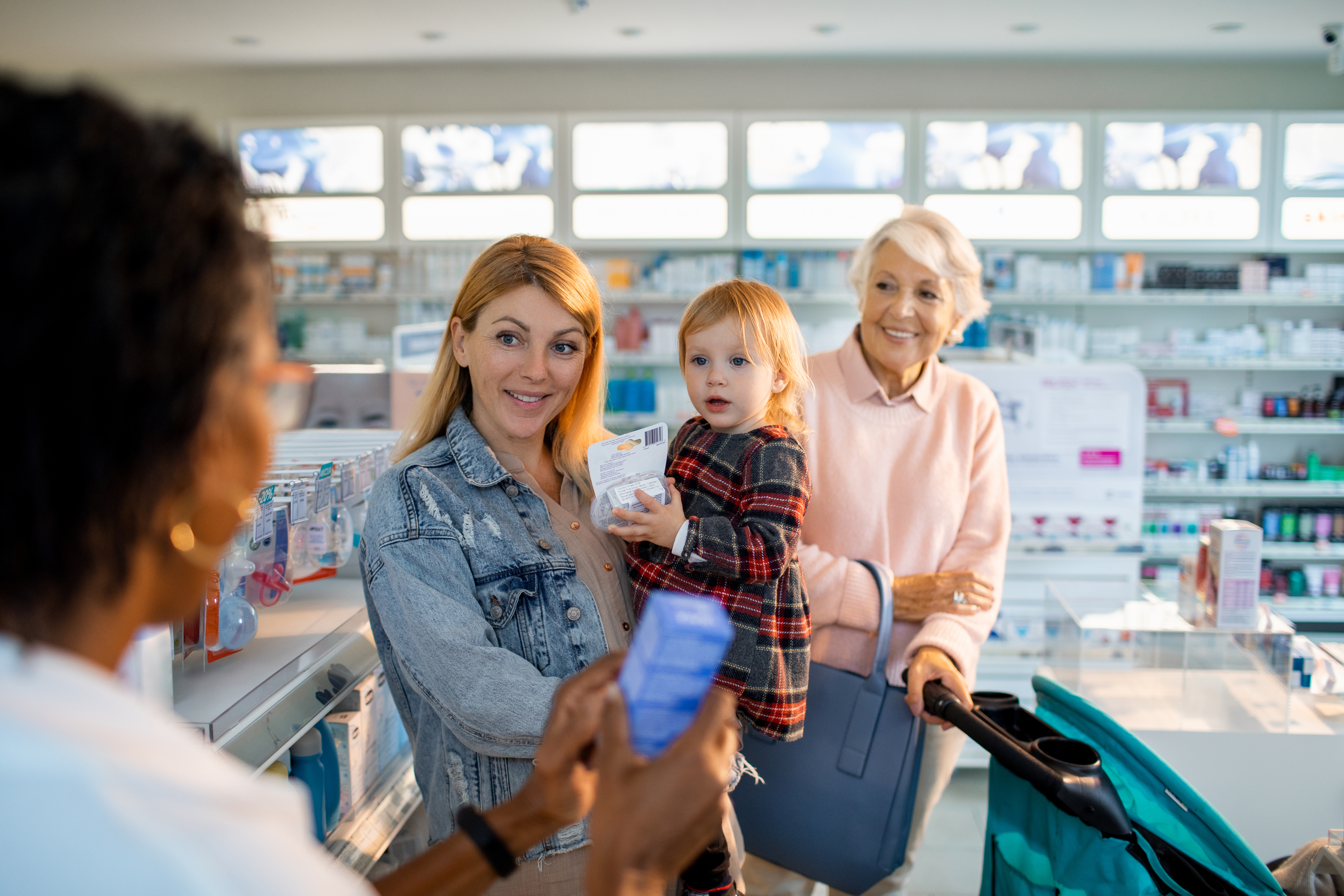 Family of young woman carrying her child in her left arm and old woman looking at the pharmacist