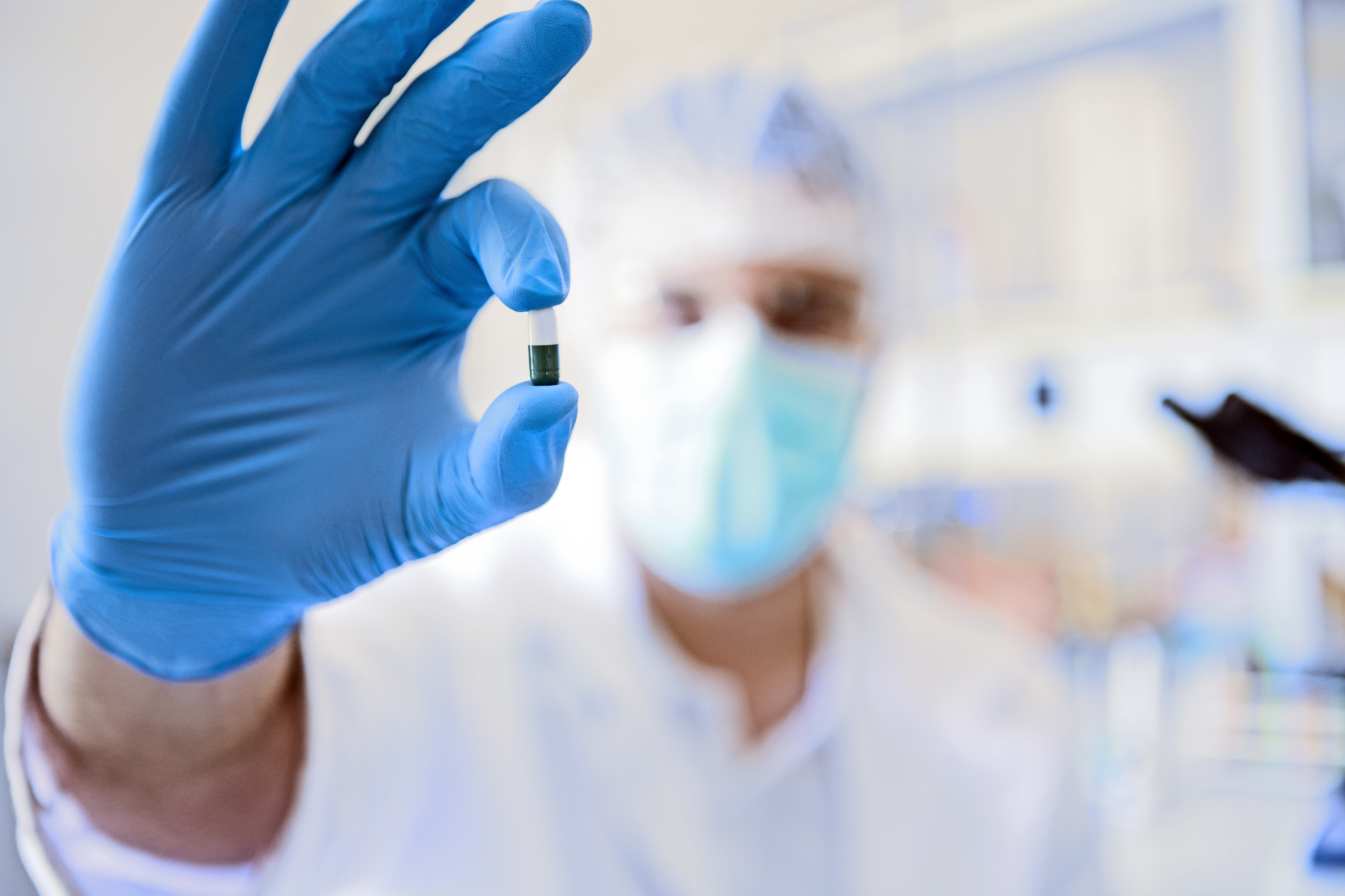 Pharmacist showing a pill with his gloves covered right hand two fingers